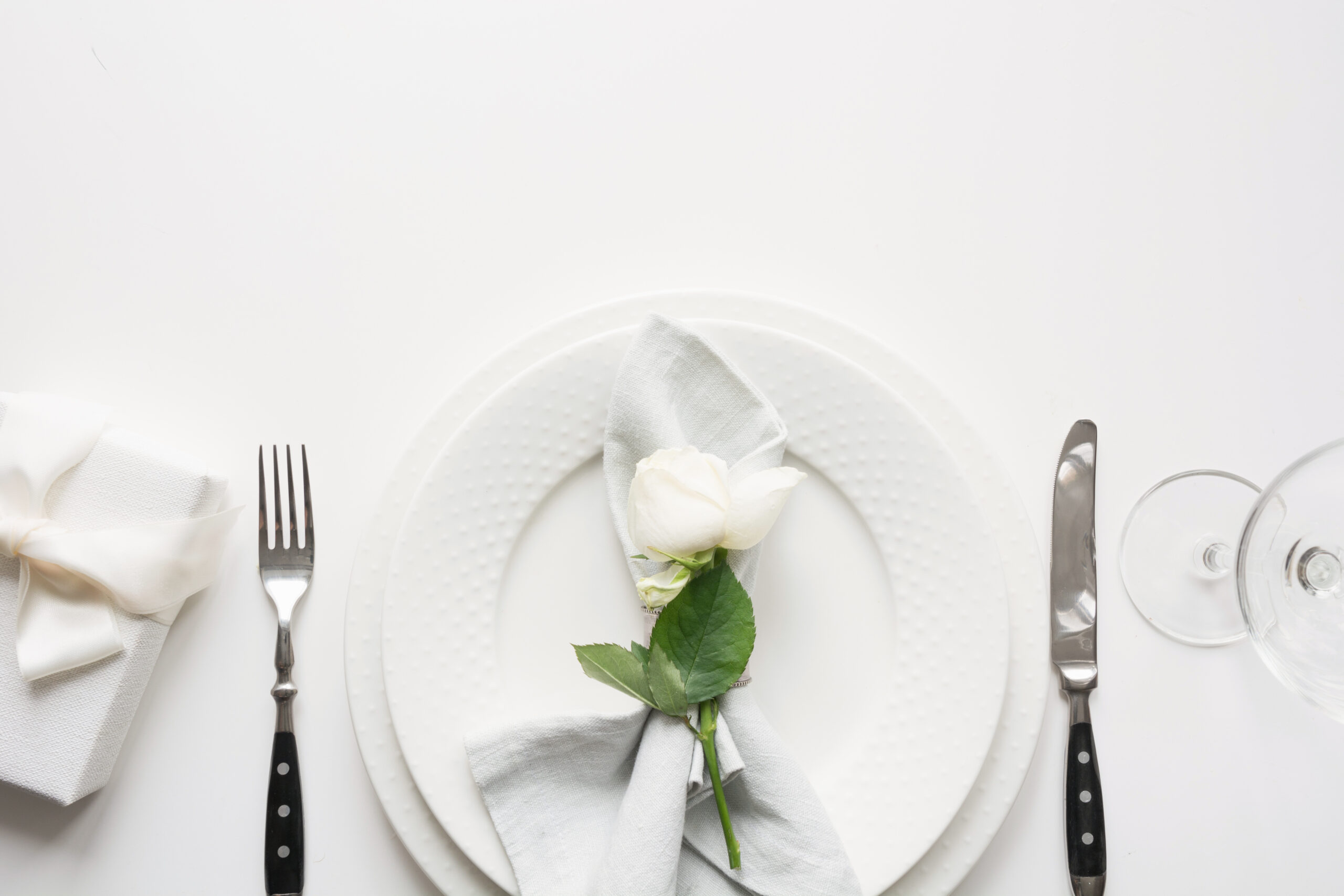 White table setting with bouquet rose, gift, dishware, silverware on holiday white table. View from above. Romantic and wedding anniversary.