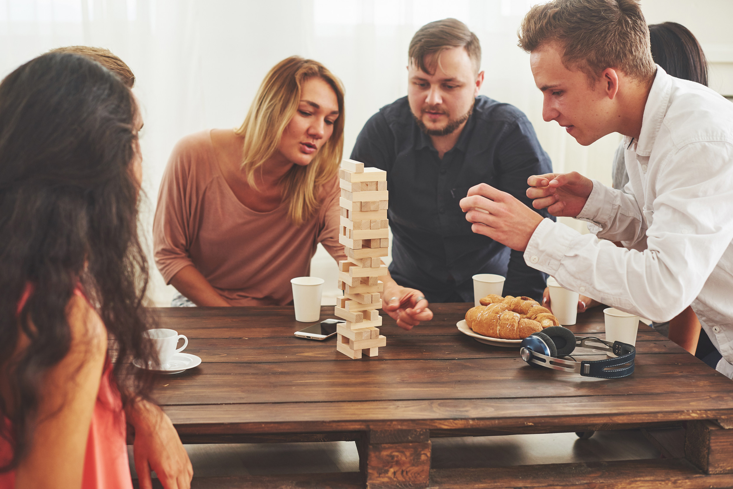 Group of creative friends sitting at wooden table. People having fun while playing board game.