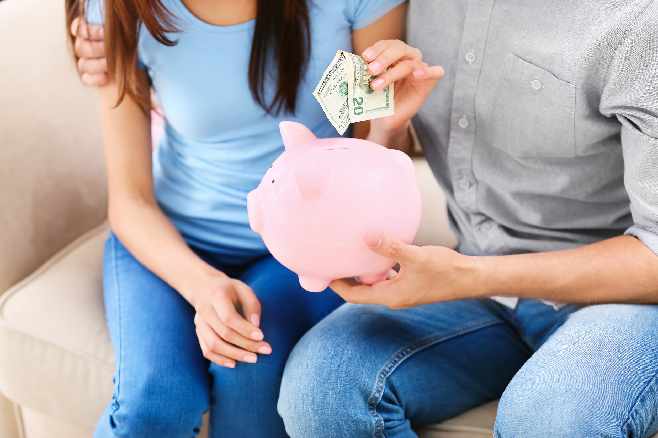 Young couple putting money into piggy bank at home