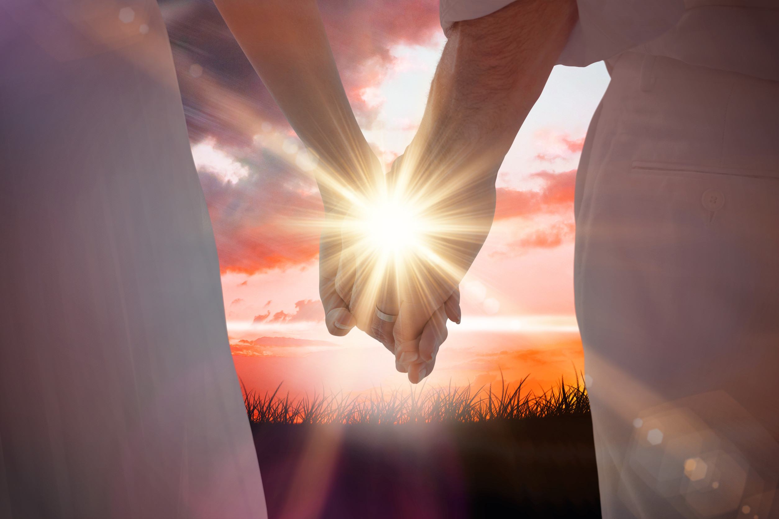 Bride and groom holding hands close up against sunrise over grass