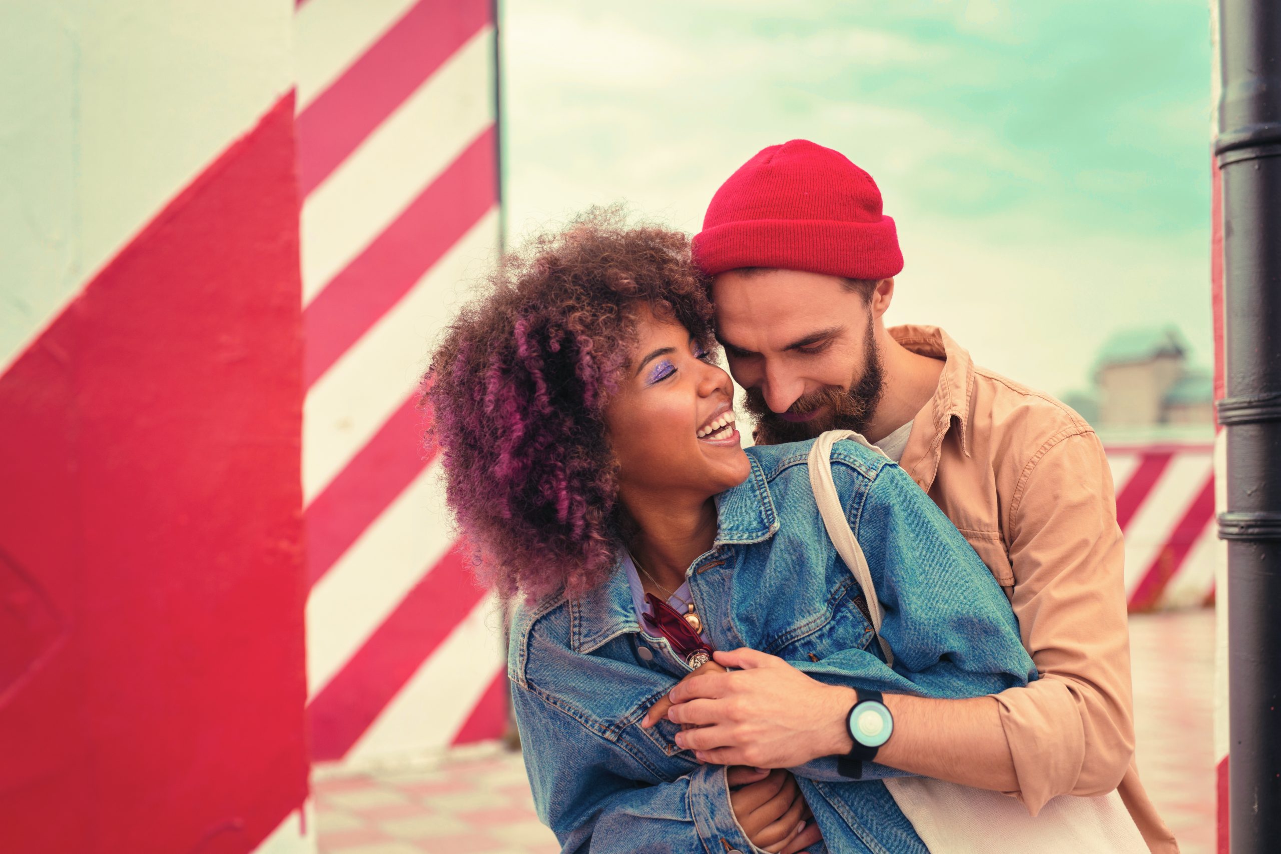 Sweet hug. Handsome bearded man kindly smiling and hugging his happy cheerful girlfriend while standing behind her back