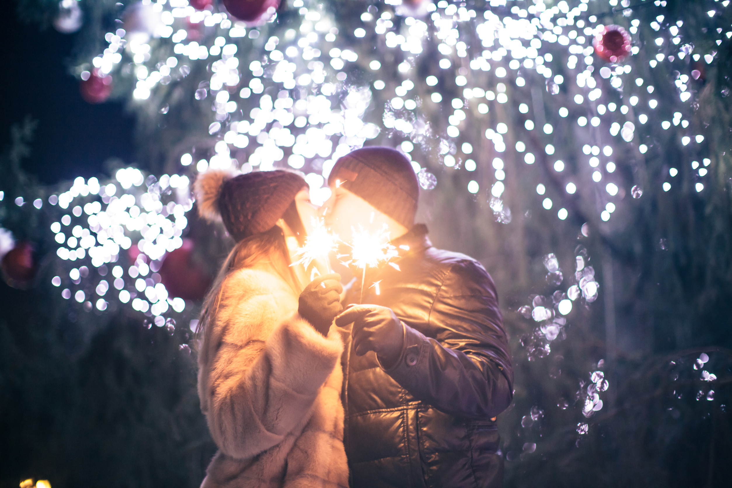 Loving couple with sparkling bengal light kissing near a Christmas tree